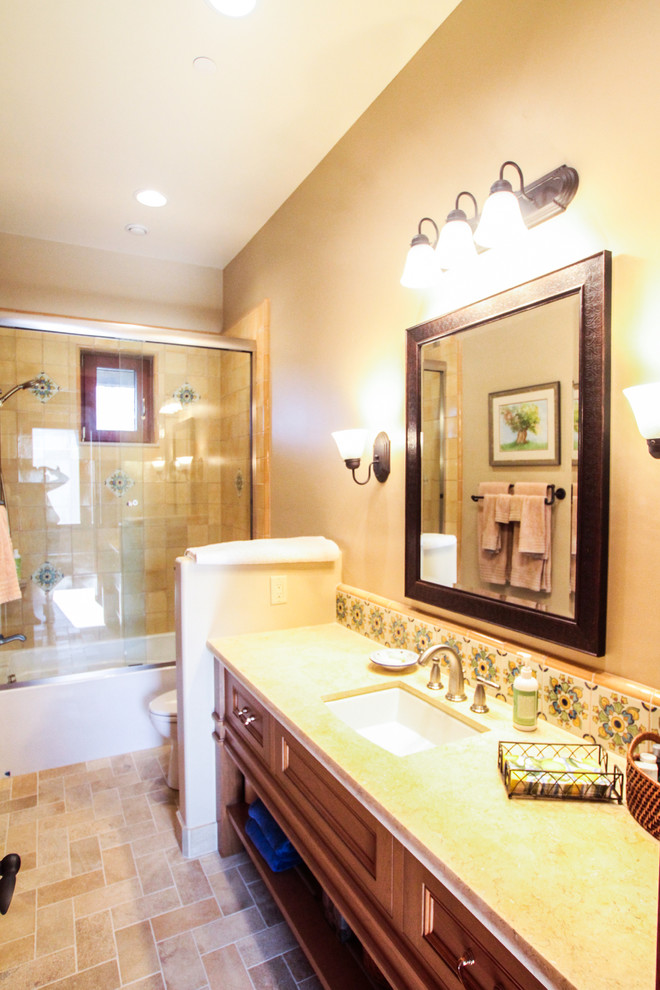 This is an example of a medium sized mediterranean ensuite bathroom in San Francisco with shaker cabinets, medium wood cabinets, an alcove bath, a shower/bath combination, a two-piece toilet, beige tiles, stone tiles, beige walls, travertine flooring, a submerged sink, granite worktops, beige floors and a sliding door.