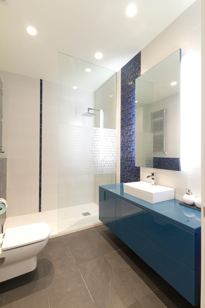 На фото: ванная комната среднего размера в стиле модернизм с плоскими фасадами, синими фасадами, открытым душем, унитазом-моноблоком, синей плиткой, керамической плиткой, белыми стенами, полом из керамической плитки, душевой кабиной, настольной раковиной, столешницей из дерева и серым полом