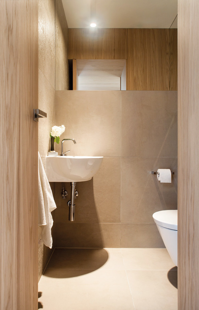 Foto på ett litet funkis badrum, med en vägghängd toalettstol, beige kakel, porslinskakel, beige väggar, klinkergolv i porslin, ett väggmonterat handfat och beiget golv