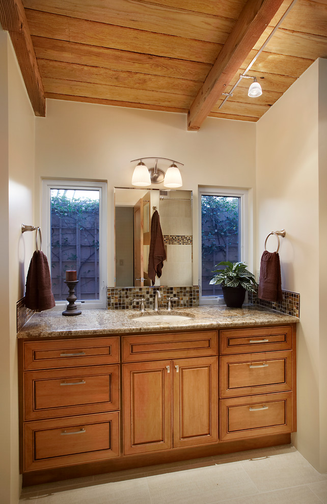 Inspiration pour une salle de bain sud-ouest américain en bois brun avec un lavabo encastré, un placard avec porte à panneau surélevé, un plan de toilette en granite, un carrelage beige, un mur beige et un sol en carrelage de porcelaine.