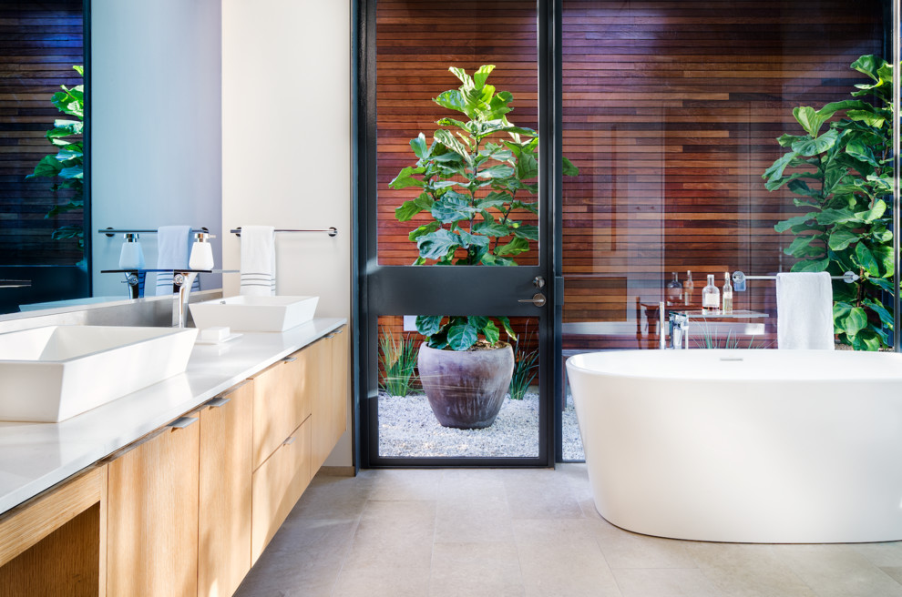 Идея дизайна: огромная главная ванная комната в современном стиле с плоскими фасадами, светлыми деревянными фасадами, отдельно стоящей ванной, угловым душем, биде, цементной плиткой, полом из известняка, настольной раковиной и столешницей из кварцита