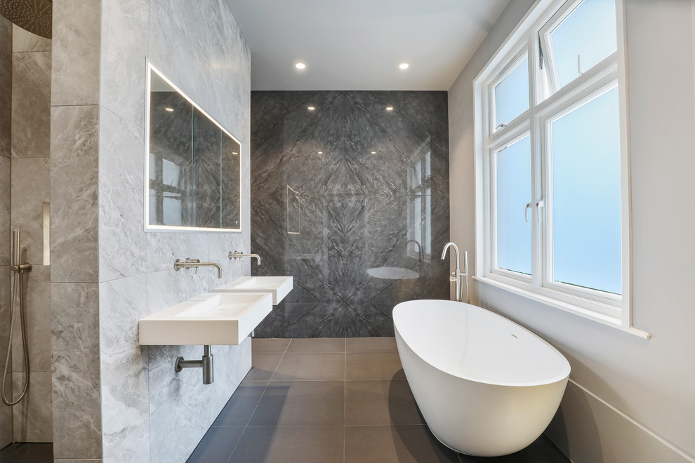 Modernes Badezimmer En Suite mit freistehender Badewanne, bodengleicher Dusche, grauen Fliesen, Wandwaschbecken, grauem Boden, offener Dusche und weißer Waschtischplatte in London