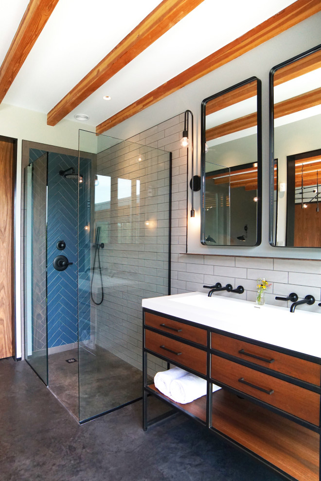 Retro inredning av ett badrum med dusch, med skåp i mellenmörkt trä, en hörndusch, blå kakel, vit kakel, tunnelbanekakel, grå väggar, ett avlångt handfat, grått golv, med dusch som är öppen, betonggolv och släta luckor
