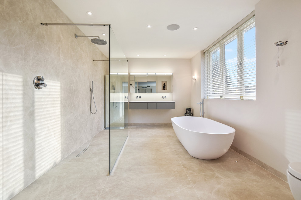 Photo of a contemporary wet room bathroom in Surrey with flat-panel cabinets, grey cabinets, a freestanding bath, beige tiles, beige walls, beige floors, an open shower and white worktops.