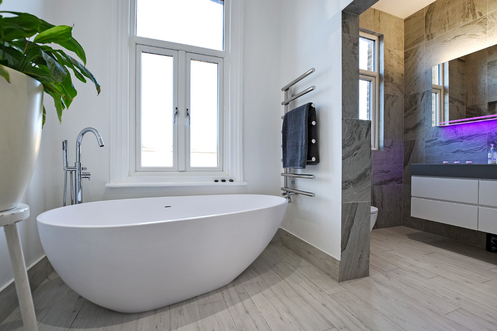 Inredning av ett modernt stort badrum, med ett fristående badkar, våtrum, en vägghängd toalettstol, grå kakel, grå väggar, ett väggmonterat handfat, beiget golv och dusch med gångjärnsdörr