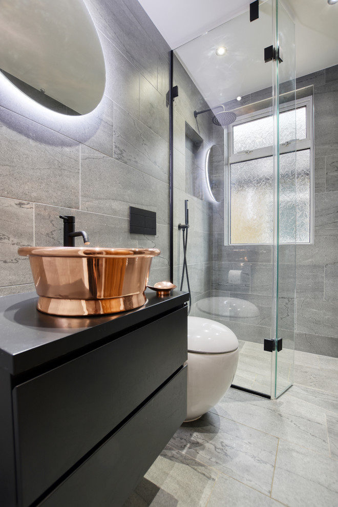 Modernes Duschbad mit flächenbündigen Schrankfronten, schwarzen Schränken, Duschnische, Toilette mit Aufsatzspülkasten, grauen Fliesen, Aufsatzwaschbecken, grauem Boden, Falttür-Duschabtrennung und schwarzer Waschtischplatte in Surrey