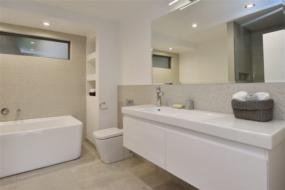 Photo of a medium sized contemporary shower room bathroom in Christchurch with white cabinets, a freestanding bath, a walk-in shower, a one-piece toilet, beige tiles, grey walls, ceramic flooring, a pedestal sink, brown floors and a hinged door.