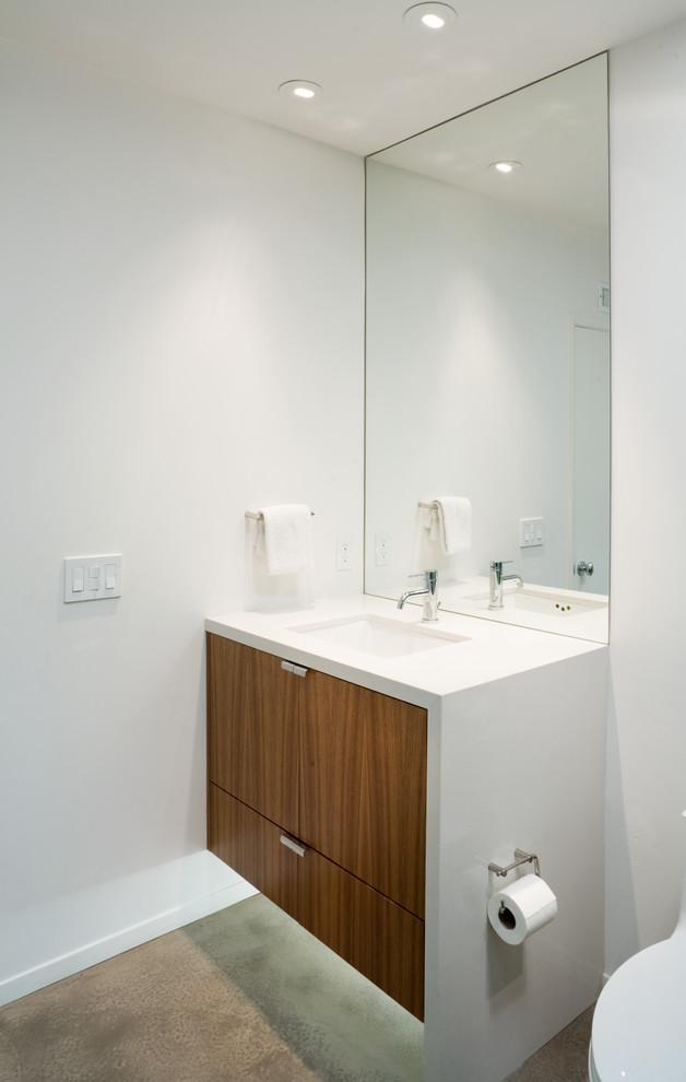 Inredning av ett retro litet badrum, med ett undermonterad handfat, släta luckor, skåp i mellenmörkt trä, bänkskiva i kvarts, en öppen dusch, en toalettstol med hel cisternkåpa, glaskakel, vita väggar och betonggolv
