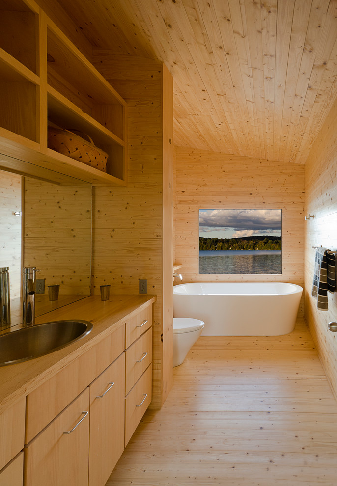 Uriges Badezimmer mit flächenbündigen Schrankfronten, hellen Holzschränken, freistehender Badewanne, hellem Holzboden, Einbauwaschbecken und Waschtisch aus Holz in Sonstige