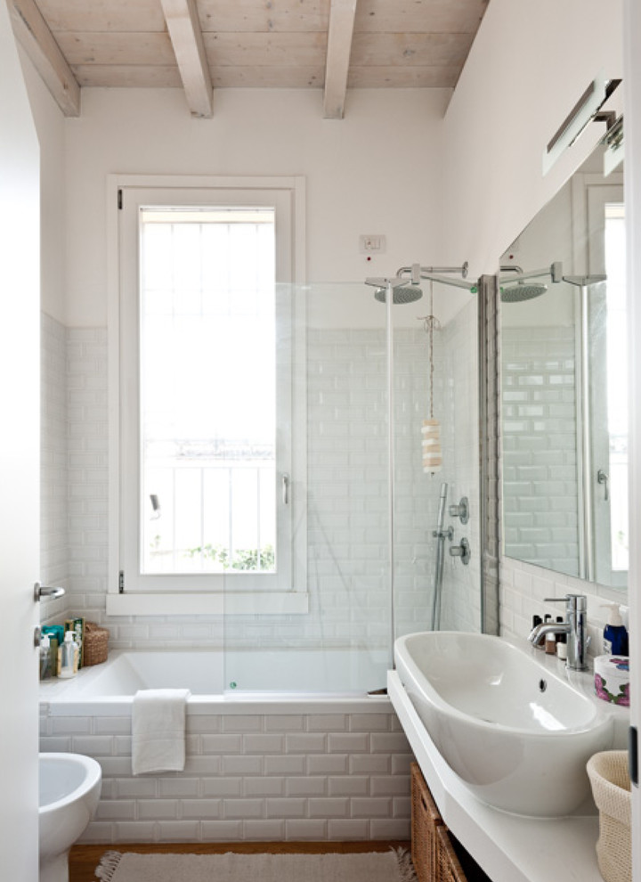 Modelo de cuarto de baño tradicional con bañera empotrada, combinación de ducha y bañera, baldosas y/o azulejos blancos, baldosas y/o azulejos de cemento, paredes blancas, lavabo sobreencimera y ventanas