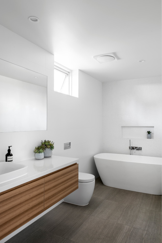 Стильный дизайн: ванная комната в современном стиле с плоскими фасадами, фасадами цвета дерева среднего тона, отдельно стоящей ванной, белой плиткой, плиткой мозаикой, накладной раковиной, серым полом, белой столешницей и подвесной тумбой - последний тренд