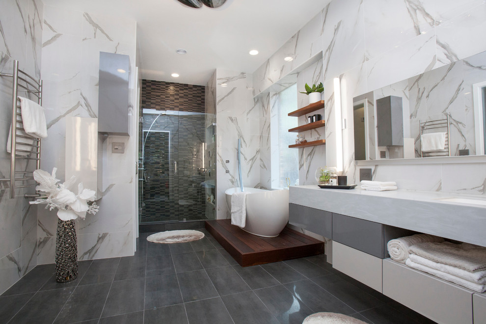 Стильный дизайн: большая главная ванная комната в современном стиле с плоскими фасадами, белыми фасадами, гидромассажной ванной, унитазом-моноблоком, серой плиткой, керамогранитной плиткой, полом из керамогранита, накладной раковиной, столешницей из известняка и белыми стенами - последний тренд