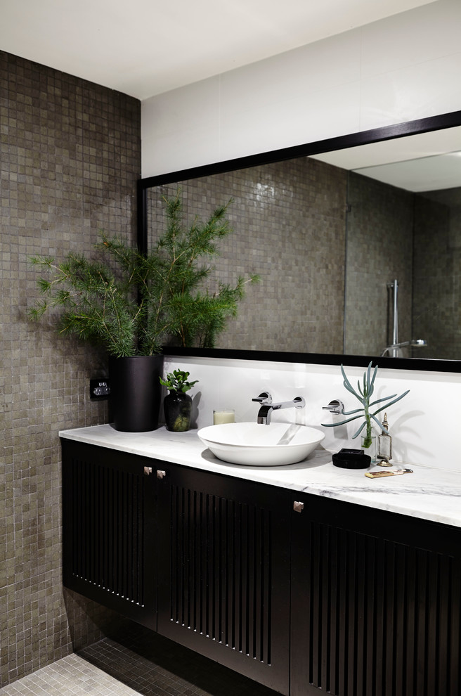 Exemple d'une salle de bain tendance avec une vasque, des portes de placard noires et un carrelage gris.