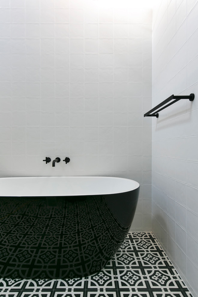 Cette photo montre une salle de bain principale tendance avec une baignoire indépendante, un mur blanc et un sol noir.