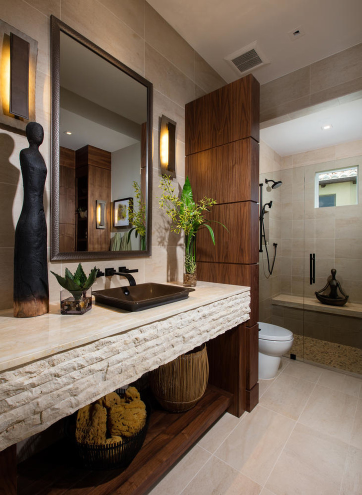 Inredning av ett modernt badrum, med öppna hyllor, skåp i mörkt trä, en kantlös dusch, beige kakel, beige väggar, ett fristående handfat och beiget golv