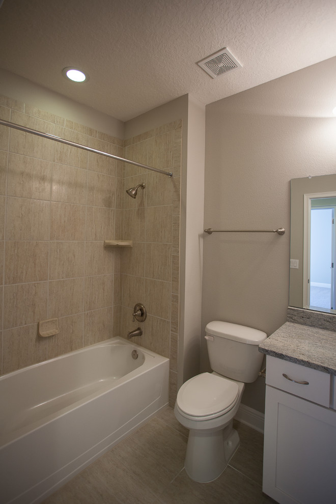 This is an example of a mediterranean bathroom in Tampa with a submerged sink, shaker cabinets, white cabinets, granite worktops, an alcove bath, a shower/bath combination, a two-piece toilet, multi-coloured tiles and porcelain tiles.