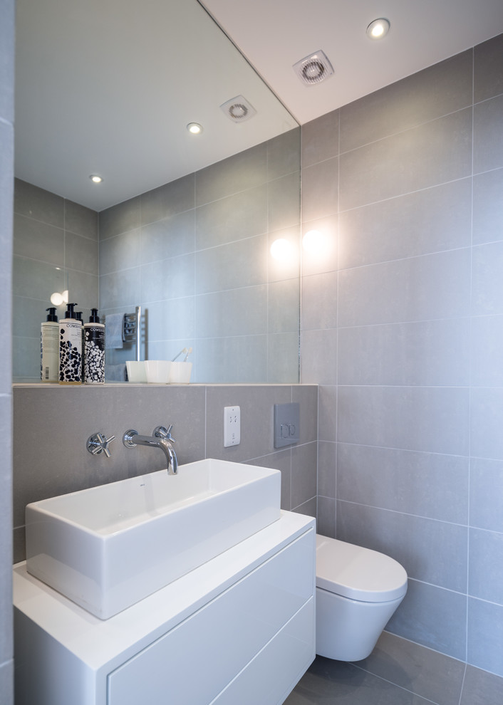Идея дизайна: серо-белая ванная комната в современном стиле с настольной раковиной, плоскими фасадами, белыми фасадами, инсталляцией, серой плиткой и серыми стенами