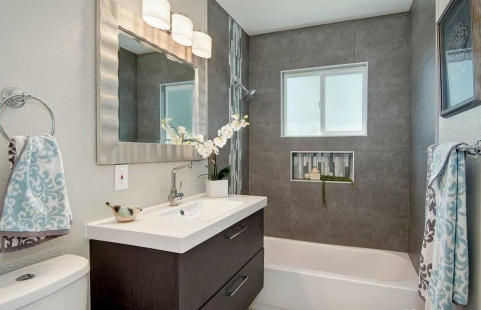Exemple d'une salle de bain principale tendance en bois foncé de taille moyenne avec un placard en trompe-l'oeil, une baignoire en alcôve, un carrelage gris, des carreaux de porcelaine, un mur gris, un sol en carrelage de porcelaine, un lavabo intégré et un plan de toilette en surface solide.