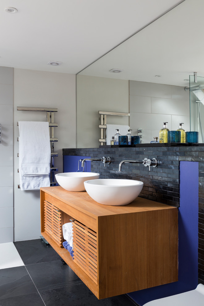 Photo of a contemporary ensuite bathroom in London with open cabinets, medium wood cabinets, a vessel sink and black floors.