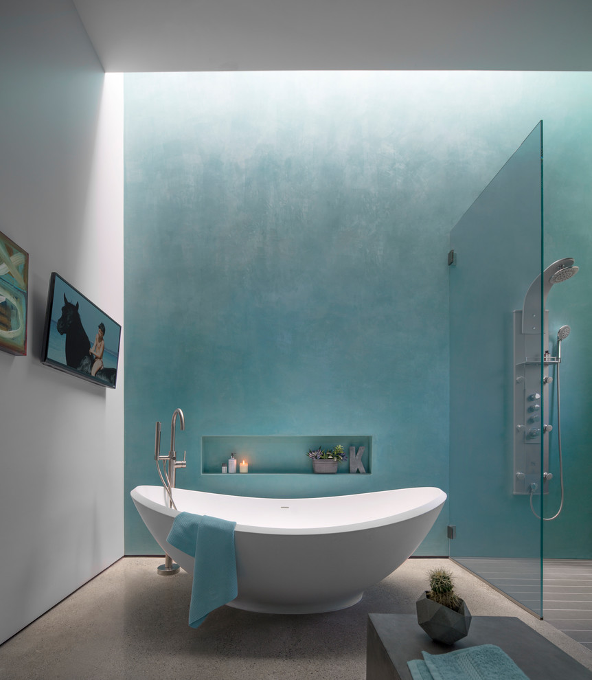 Cette image montre une salle de bain design avec une baignoire indépendante, une douche à l'italienne, un mur bleu, sol en béton ciré et un sol gris.