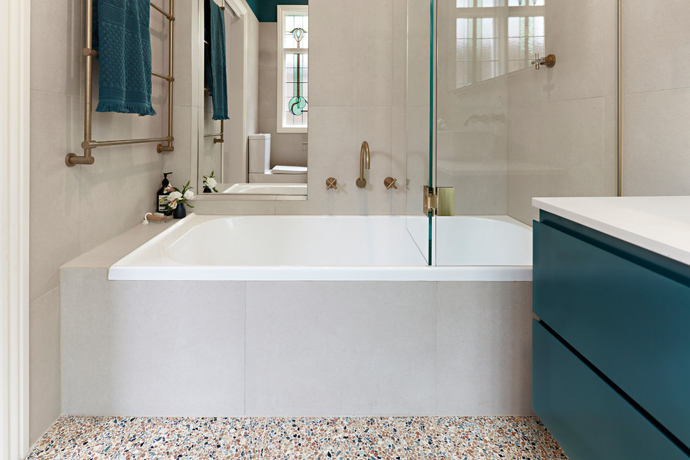 На фото: маленькая главная ванная комната в современном стиле с зелеными фасадами, душем над ванной, бежевой плиткой, полом из терраццо, душем с распашными дверями, белой столешницей, фасадами островного типа, накладной ванной, инсталляцией, каменной плиткой, бежевыми стенами, настольной раковиной, столешницей из искусственного кварца и разноцветным полом для на участке и в саду с