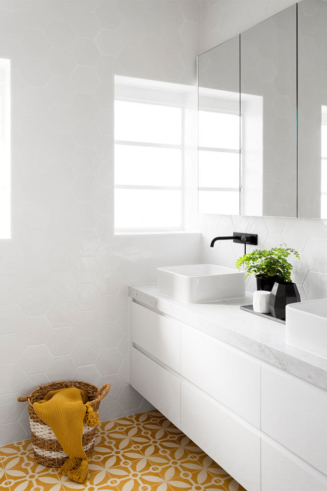 Large contemporary ensuite bathroom in Melbourne with flat-panel cabinets, white cabinets, a built-in bath, a corner shower, a one-piece toilet, white tiles, ceramic tiles, white walls, cement flooring, a vessel sink, marble worktops, yellow floors and a hinged door.