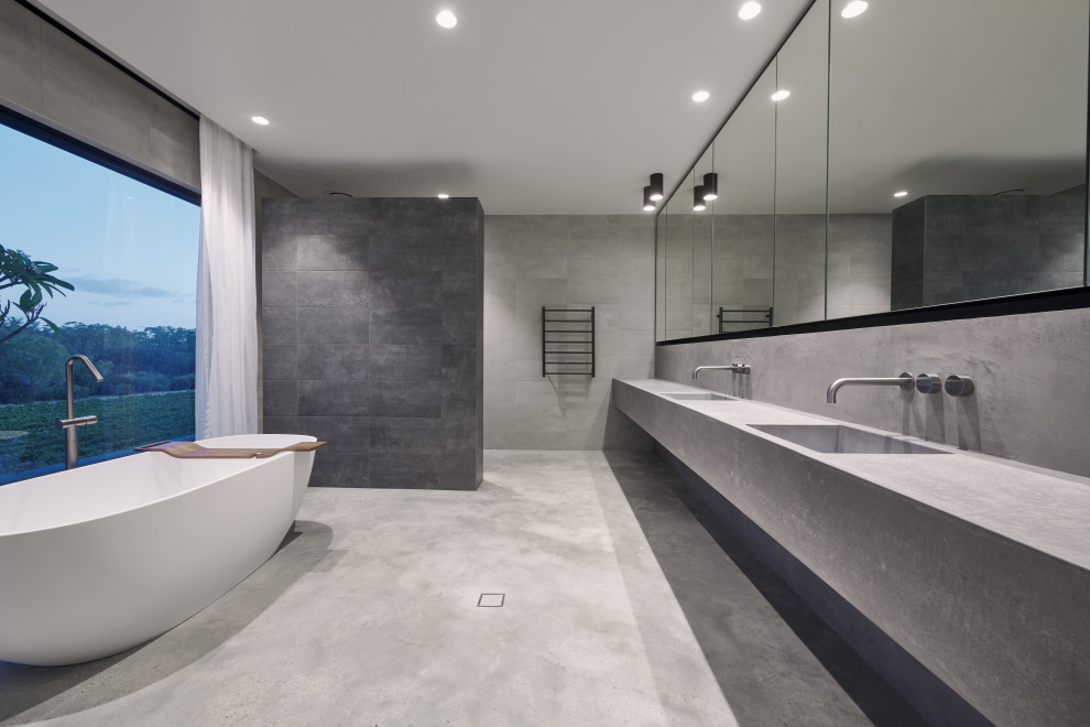 Идея дизайна: большая главная ванная комната в стиле модернизм с серыми фасадами, отдельно стоящей ванной, серой плиткой, плиткой из листового камня, серыми стенами, бетонным полом, столешницей из бетона, серым полом, открытым душем, серой столешницей, тумбой под две раковины, душем без бортиков, монолитной раковиной и подвесной тумбой