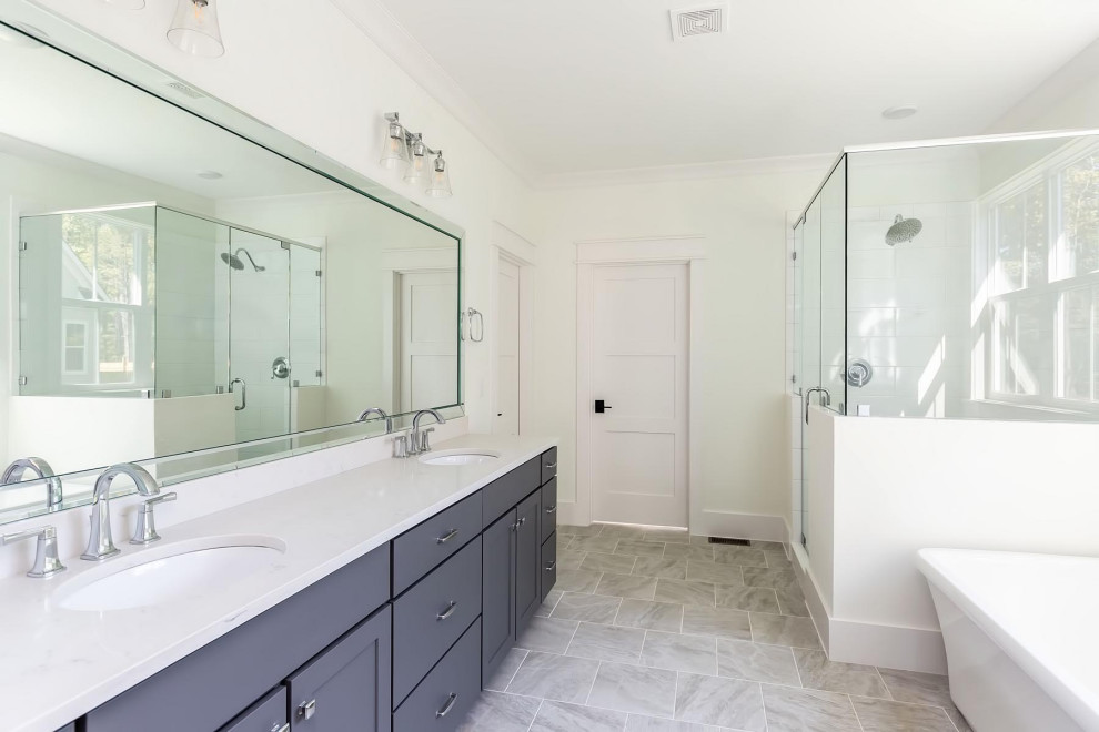 Пример оригинального дизайна: большая главная ванная комната в классическом стиле с фасадами в стиле шейкер, серыми фасадами, отдельно стоящей ванной, душем в нише, раздельным унитазом, белой плиткой, керамической плиткой, серыми стенами, полом из керамической плитки, врезной раковиной, столешницей из искусственного кварца, серым полом, душем с распашными дверями и бежевой столешницей