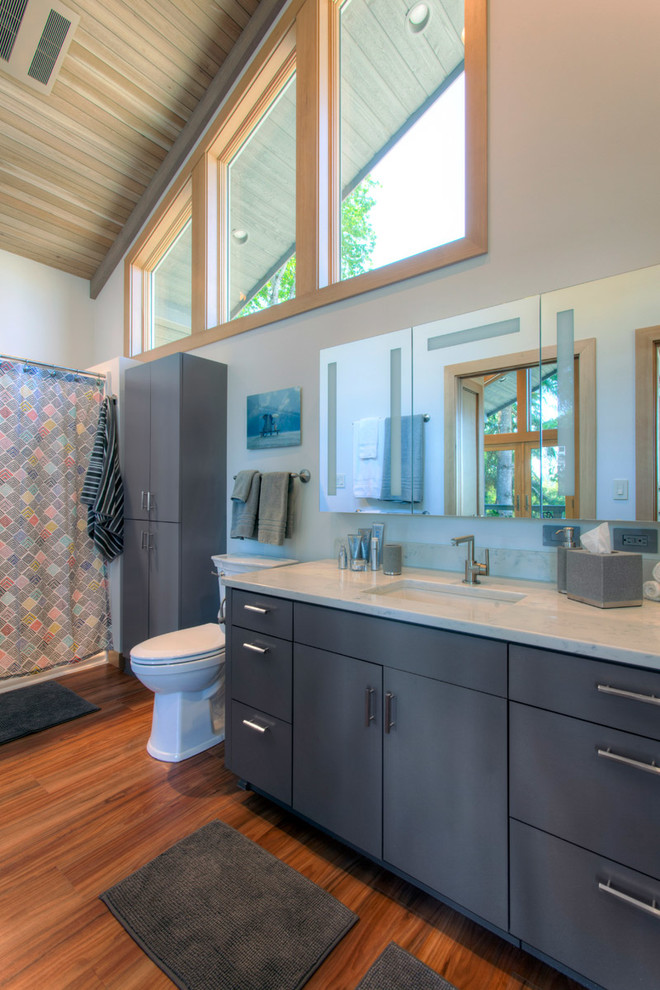 Photo of a medium sized classic ensuite bathroom in Portland with flat-panel cabinets, blue cabinets, an alcove bath, a shower/bath combination, a two-piece toilet, grey walls, medium hardwood flooring, a submerged sink, engineered stone worktops and a shower curtain.