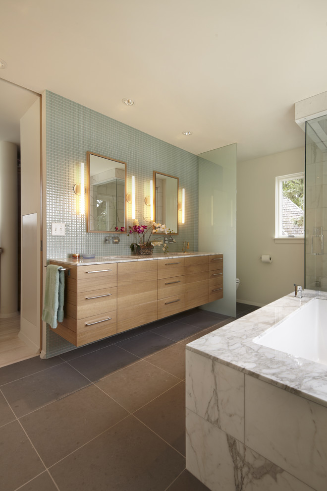 На фото: ванная комната в современном стиле с врезной раковиной, плоскими фасадами, полновстраиваемой ванной, серой плиткой и светлыми деревянными фасадами