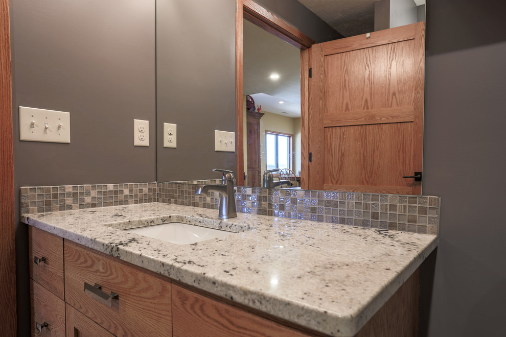 Cette image montre une petite salle de bain craftsman en bois brun avec un placard avec porte à panneau encastré, un carrelage multicolore, un carrelage en pâte de verre, un mur violet, un sol en carrelage de porcelaine, un lavabo encastré et un plan de toilette en granite.