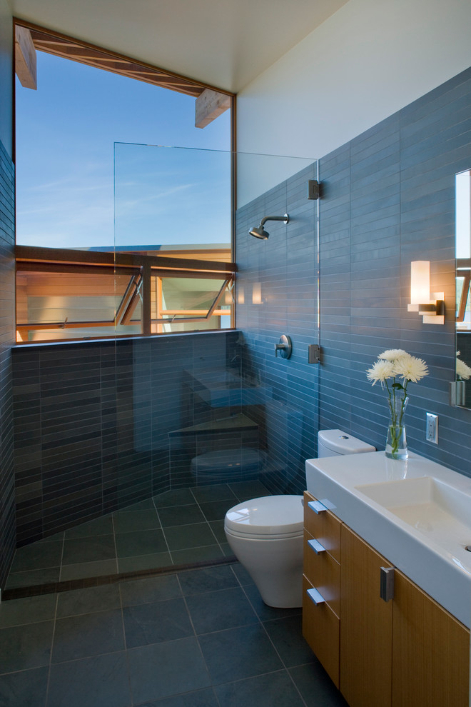 Immagine di una grande stanza da bagno minimal con lavabo integrato, ante lisce, ante in legno scuro, doccia aperta, WC monopezzo, piastrelle nere e piastrelle in pietra