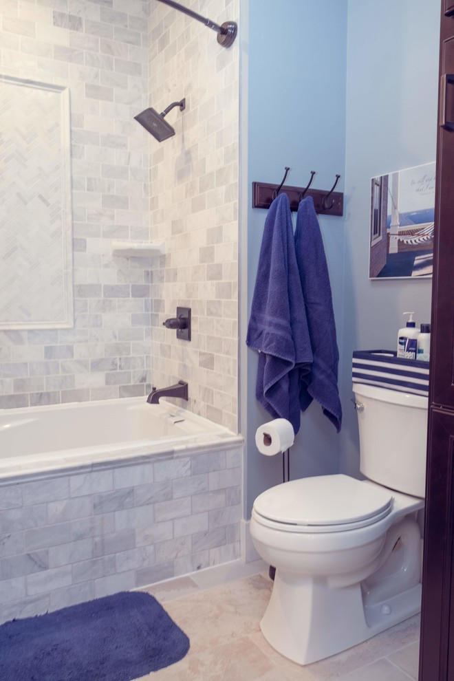Photo of a traditional ensuite bathroom in Cedar Rapids with recessed-panel cabinets, dark wood cabinets, a built-in bath, a shower/bath combination, a two-piece toilet, white tiles, marble tiles, blue walls, porcelain flooring, an integrated sink, solid surface worktops, white floors, a shower curtain and white worktops.