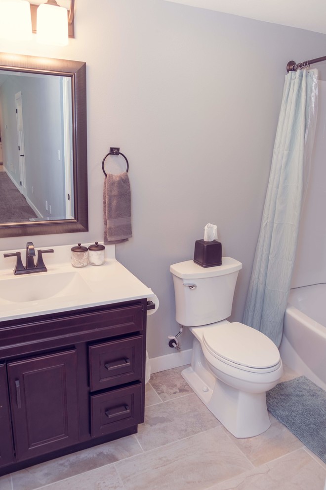 This is an example of a classic bathroom in Cedar Rapids with recessed-panel cabinets, dark wood cabinets, an alcove bath, a shower/bath combination, a two-piece toilet, marble tiles, porcelain flooring, an integrated sink, solid surface worktops, white floors, a shower curtain and white worktops.