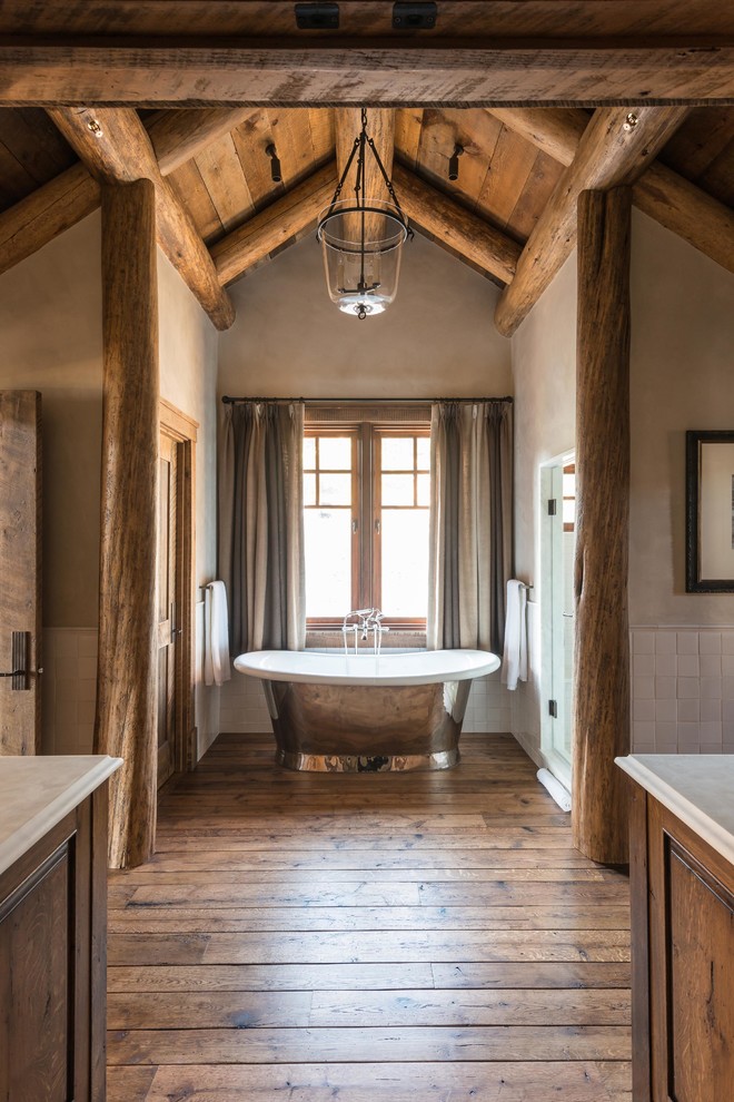 Foto de cuarto de baño rústico con bañera exenta, baldosas y/o azulejos blancos, paredes beige y suelo de madera en tonos medios