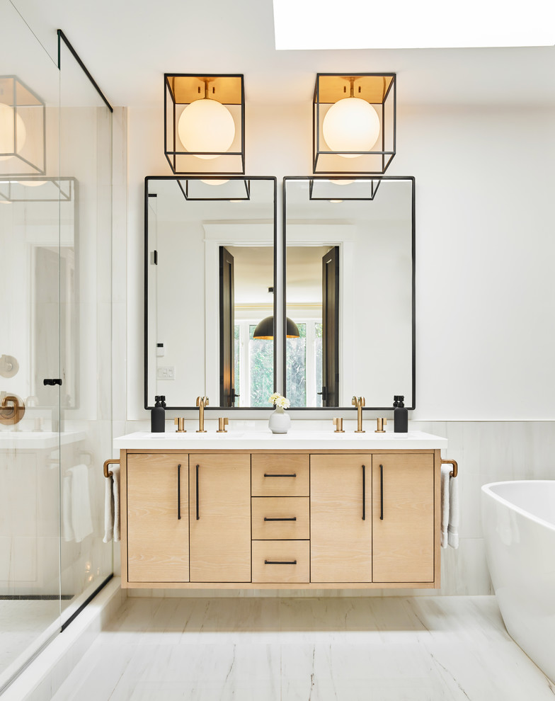 На фото: главная ванная комната в скандинавском стиле с плоскими фасадами, светлыми деревянными фасадами, отдельно стоящей ванной, белыми стенами, белым полом, белой столешницей и зеркалом с подсветкой с