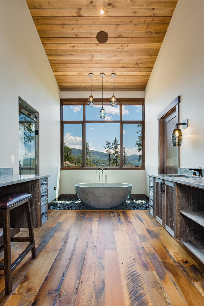 Réalisation d'une grande salle de bain principale chalet en bois vieilli avec un sol en bois brun, un lavabo encastré, un plan de toilette en granite, un plan de toilette gris et une baignoire indépendante.