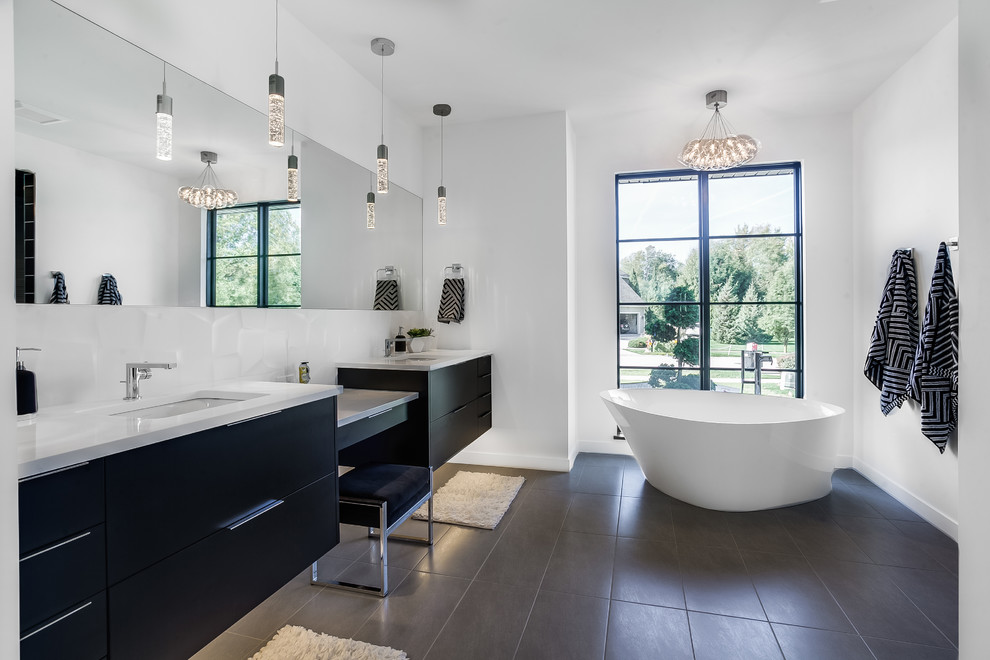 Стильный дизайн: главная ванная комната в современном стиле с плоскими фасадами, черными фасадами, отдельно стоящей ванной, душем в нише, черной плиткой, белыми стенами, врезной раковиной, серым полом, белой столешницей и зеркалом с подсветкой - последний тренд