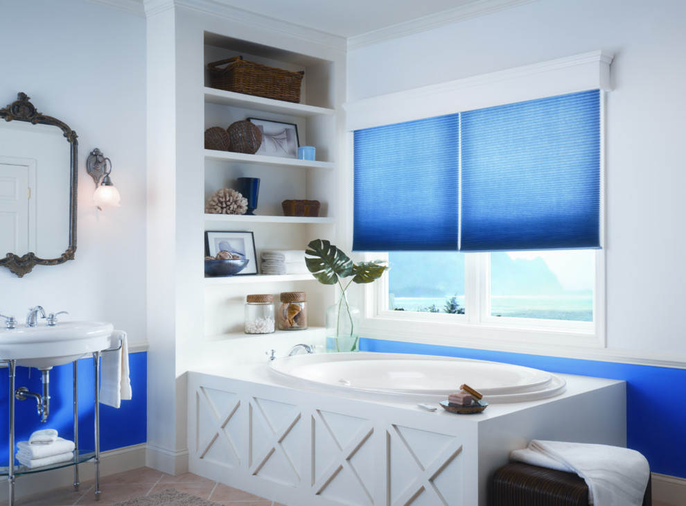 Modelo de cuarto de baño principal actual de tamaño medio con armarios abiertos, bañera esquinera, paredes azules, suelo de travertino, lavabo suspendido, encimera de acrílico y suelo beige