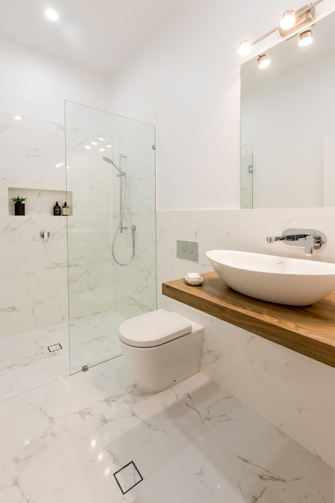На фото: ванная комната в современном стиле с унитазом-моноблоком, настольной раковиной, фасадами цвета дерева среднего тона, белой плиткой, душем без бортиков и открытым душем