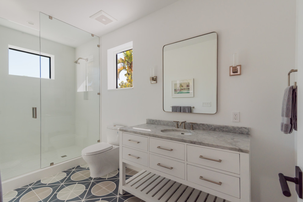 Exempel på ett mellanstort maritimt grå grått badrum med dusch, med vita skåp, en dusch i en alkov, en toalettstol med separat cisternkåpa, vita väggar, ett undermonterad handfat, flerfärgat golv, dusch med gångjärnsdörr och släta luckor
