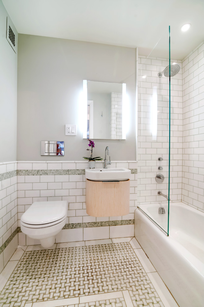Idéer för ett litet modernt badrum, med skåp i ljust trä, en vägghängd toalettstol, vit kakel, ett väggmonterat handfat, ett badkar i en alkov, en dusch/badkar-kombination, tunnelbanekakel, mosaikgolv, grå väggar och släta luckor