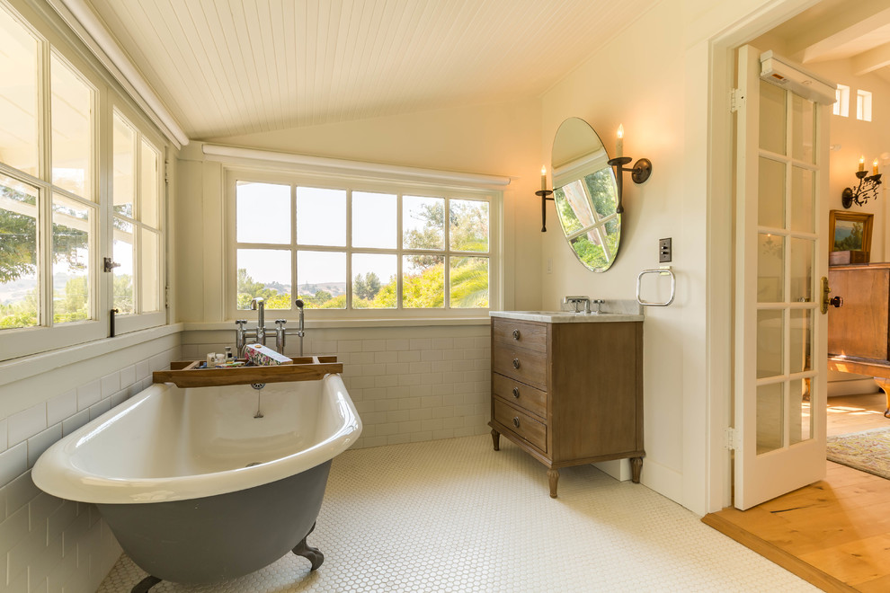 Aménagement d'une salle de bain campagne en bois brun avec une baignoire sur pieds, un carrelage beige, un mur beige, un sol en carrelage de terre cuite, un lavabo encastré, un sol beige, un plan de toilette gris et un placard à porte plane.