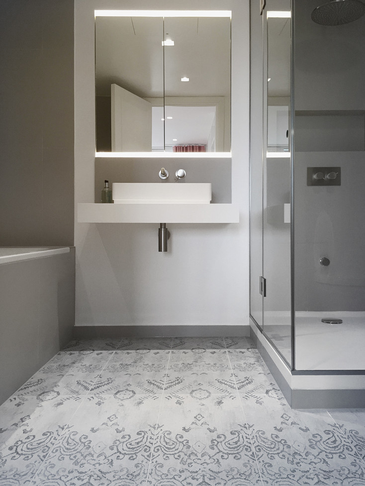 Photo of a medium sized contemporary ensuite bathroom in London with flat-panel cabinets, white cabinets, a built-in bath, a corner shower, a wall mounted toilet, blue tiles, ceramic tiles, grey walls, ceramic flooring, a trough sink and engineered stone worktops.