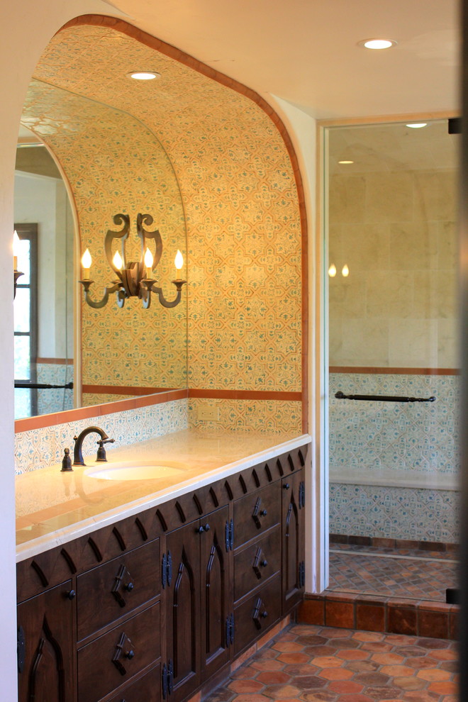 サンディエゴにあるラグジュアリーな巨大な地中海スタイルのおしゃれなマスターバスルーム (アンダーカウンター洗面器、落し込みパネル扉のキャビネット、濃色木目調キャビネット、大理石の洗面台、置き型浴槽、ダブルシャワー、分離型トイレ、マルチカラーのタイル、テラコッタタイル、白い壁、コンクリートの床) の写真