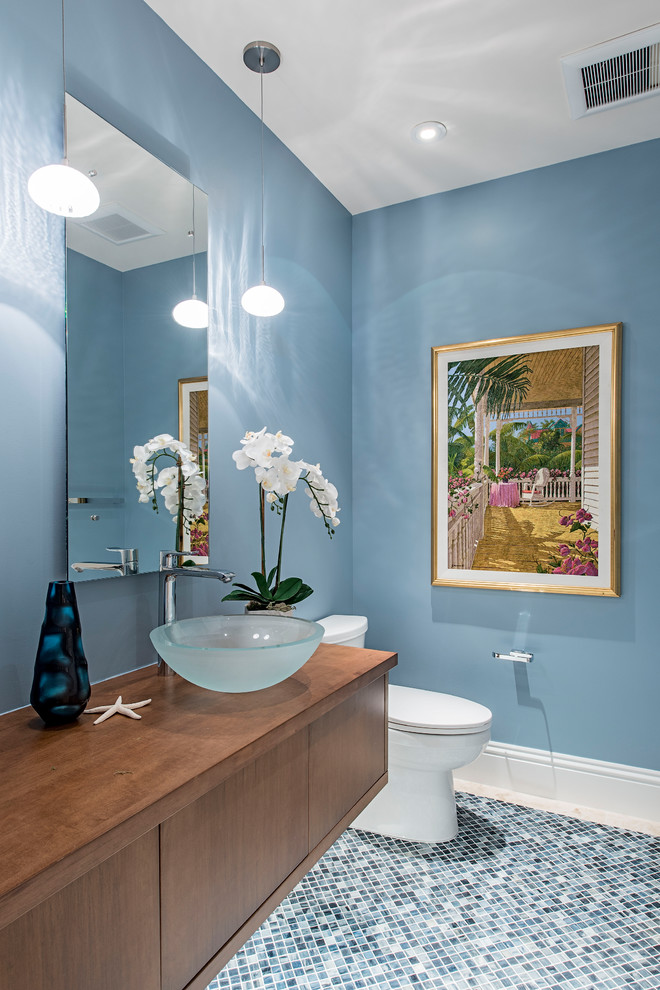 Beach style mosaic tile floor and blue floor bathroom photo in Kansas City with flat-panel cabinets, medium tone wood cabinets, a two-piece toilet, blue walls, a vessel sink, wood countertops and brown countertops
