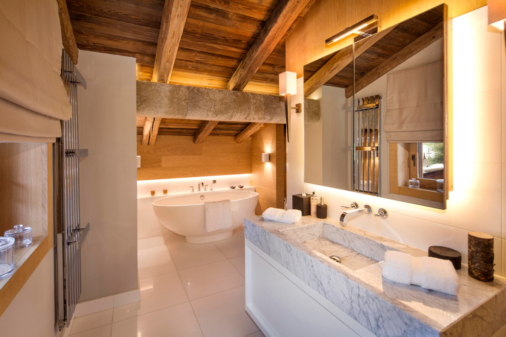 Freestanding bathtub - rustic single-sink, white floor, exposed beam, vaulted ceiling and wood ceiling freestanding bathtub idea in London with white cabinets, marble countertops, flat-panel cabinets, white walls, an integrated sink, gray countertops and a floating vanity