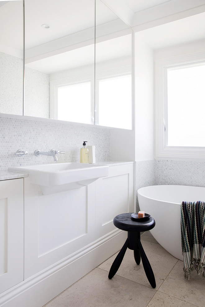 Пример оригинального дизайна: ванная комната в современном стиле с фасадами в стиле шейкер, белыми фасадами, отдельно стоящей ванной, серой плиткой, белой плиткой, плиткой мозаикой, белыми стенами, подвесной раковиной и бежевым полом