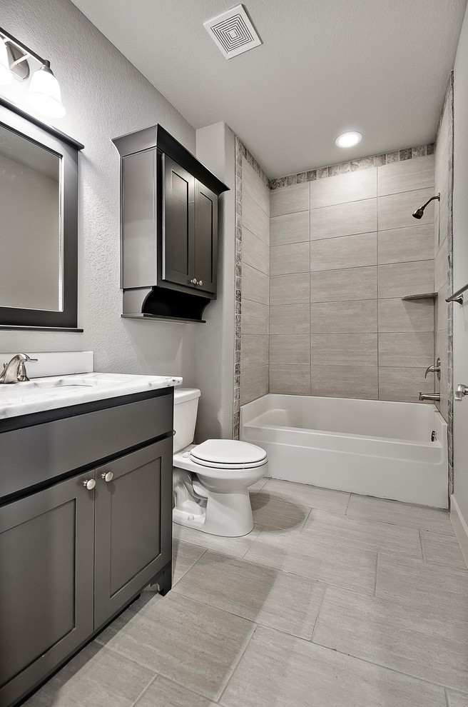 Inredning av ett klassiskt mellanstort badrum, med skåp i shakerstil, grå skåp, ett badkar i en alkov, en dusch/badkar-kombination, en toalettstol med separat cisternkåpa, beige kakel, porslinskakel, grå väggar, klinkergolv i porslin, ett undermonterad handfat, marmorbänkskiva och grått golv