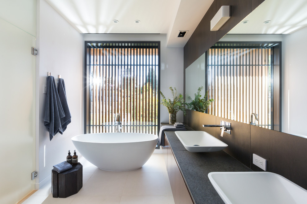 Trendy master porcelain tile freestanding bathtub photo in Vancouver with flat-panel cabinets, medium tone wood cabinets, white walls, a vessel sink, quartzite countertops and a hinged shower door